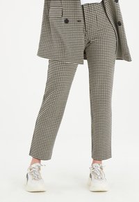 Kalhoty v černobílém houndstooth vzoru, přiléhavý střih, s bočními kapsami a zkrácenou délkou, nošené s bílými teniskami.