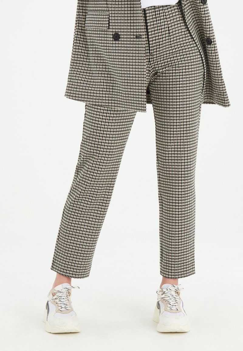 Kalhoty v černobílém houndstooth vzoru, přiléhavý střih, s bočními kapsami a zkrácenou délkou, nošené s bílými teniskami.