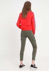 Röd sweatshirts med blå sidostråkar, i kombination med olivgröna cargobyxor med sidofickor och svarta sneakers.