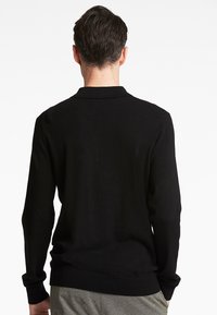 Sort langærmet polo-shirt med ribbet krave og manchetter. Glat tekstur, tætsiddende design og en kant der falder ved taljen.