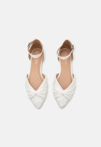 Vita, spetsiga ballerinas med ankelsnodd, prydda med en rosett och blommönster på tådelen. Slät läderliknande material.