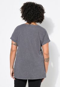 Grå kortærmet T-shirt lavet af blødt stof med en afslappet pasform. Rund halsudskæring og synlige stikninger.
