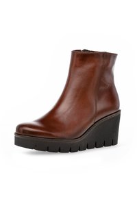 Bota de cuero marrón hasta el tobillo con punta redondeada, suela de cuña y plataforma texturizada negra. Cuenta con una cremallera lateral para un fácil uso.