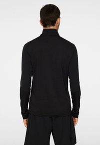 Svart långärmad träningsöverdel med ståkrage, som har en slim fit, slät textur och kontrasterande paneler på ärmarna.