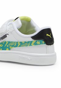 Baskets blanches avec un talon noir, panneau latéral texturé vert et jaune à motifs, dessus en cuir lisse et col légèrement rembourré.