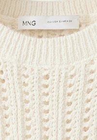 Pull en maille blanc avec un col côtelé et un motif en losanges ajouré, arborant une étiquette de vêtement blanche indiquant "MNG EU-USA S / MEX CH".