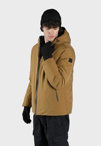 Giacca isolante marrone con cappuccio, guanti neri e berretto in maglia nera; presenta una zip frontale e tasche laterali, tessuto a trama.