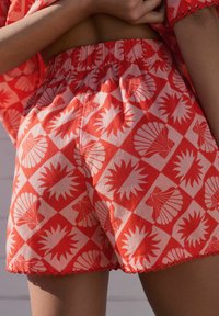 Pantaloncini rossi con motivo a conchiglia e raggi di sole, caratterizzati da una vita elastica e orlo smerlato, realizzati in tessuto leggero.