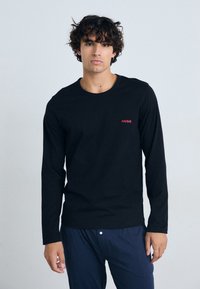 T-shirt noir à manches longues en coton avec col rond et logo rouge "HUGO" sur la poitrine. Texture lisse, design ajusté.