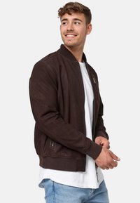 Braune Lederbomberjacke mit gerippten Bündchen und Kragen, durchgehendem Reißverschluss, seitlichen Taschen und einer strukturierten Oberfläche. Tr�ägt man über einem weißen Hemd.