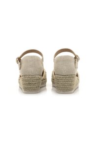 Sandalias de esparto beige con tira en el tobillo, parte superior de lona, tacón de cuña de yute trenzado y suela plana de goma. Costuras detalladas a lo largo de los bordes.