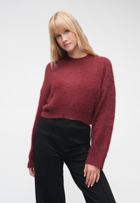 Μπουκλέ μπορντό cropped πουλόβερ με μακριά, φαρδιά μανίκια και στρογγυλή λαιμόκοψη, σετ με ψηλόμεσο μαύρο παντελόνι.