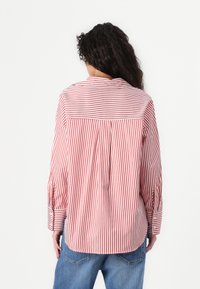 Camisa de mangas longas às riscas vermelhas e brancas com detalhe de pregas nas costas e punhos com botões, feita de tecido tecido. Corte casual, com bainha arredondada.
