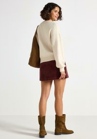 Creme sweater, maroon corduroy nederdel og brune ruskind ankelstøvler; afslappet pasform, ribbede kanter på sweateren, glat tekstur på nederdel.