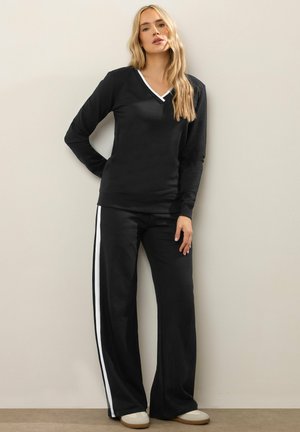Schwarzes Lounge-Set mit einem Langarmoberteil mit weißem V-Ausschnitt und lässigen Hosen mit weißen Seitenstreifen. Glatte Stoffstruktur.