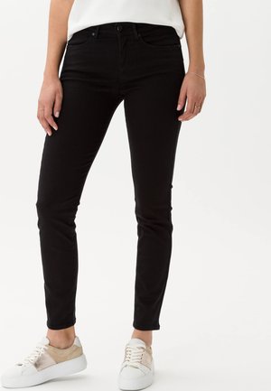 Schwarze, enge Jeans aus Denim mit hoher Taille, Fronttaschen und schmalem Bein. Kombiniert mit weißen und hellbraunen Sneakers.