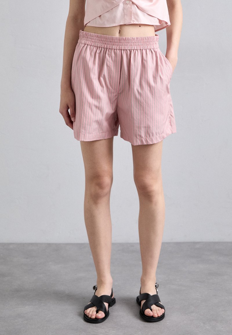 Roze gestreepte shorts met een elastische tailleband en zakken, gemaakt van lichtgewicht stof. Gecombineerd met zwarte sandalen met banden.