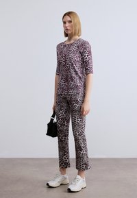 Σετ ρούχων με τύπωμα λεοπάρδαλης που αποτελείται από εφαρμοστό κοντομάνικο τοπ και παντελόνι που ταιριάζουν, και τα δύο σε αποχρώσεις του μωβ και του κρεμ, συνδυασμένα με λευκά αθλητικά παπούτσια.