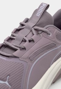 Scarpa da ginnastica viola chiaro con tomaia in rete, sovrapposizioni testurizzate e lacci piatti. Presenta una linguetta e un'etichetta sul tallone imbottite per il comfort.