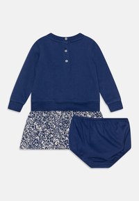 Maglia a maniche lunghe blu navy con chiusura a bottoni, abbinata a una gonna a fantasia floreale e a dei pantaloni coordinati, il tutto realizzato in tessuto morbido.