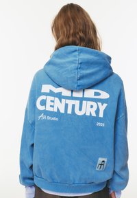 Felpa oversize azzurra con cappuccio e una grande grafica bianca con la scritta "MID CENTURY" sul retro. Presenta un cappuccio con cordino e polsini a coste.
