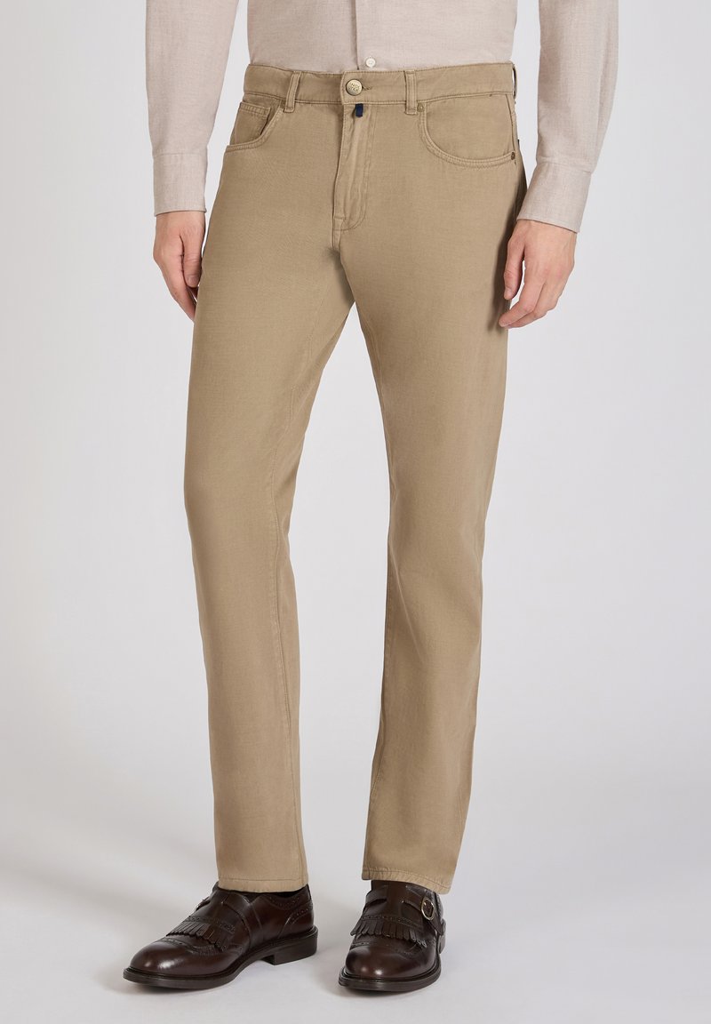 Chinos color caqui con un diseño de pierna recta, fabricados en algodón y con costuras visibles. Combinados con zapatos de vestir marrón oscuro.