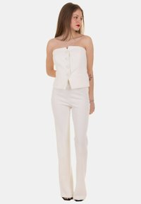 Top bianco aderente senza spalline con scollatura a V e grandi bottoni, abbinato a pantaloni bianchi a gamba dritta, che mostrano una texture liscia.