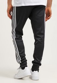 Svarta träningsbyxor med vita sidosträck, gjorda av slätt tyg, med smala fållar. Bärs med vita sneakers.