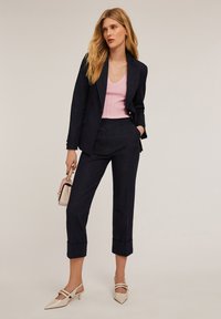 Mörkblå skräddarsydd kavaj och matchande korta byxor i kombination med en ljusrosa ribbad topp. Outfiten innehåller krämfärgade spetsiga klackar och en liten handväska.