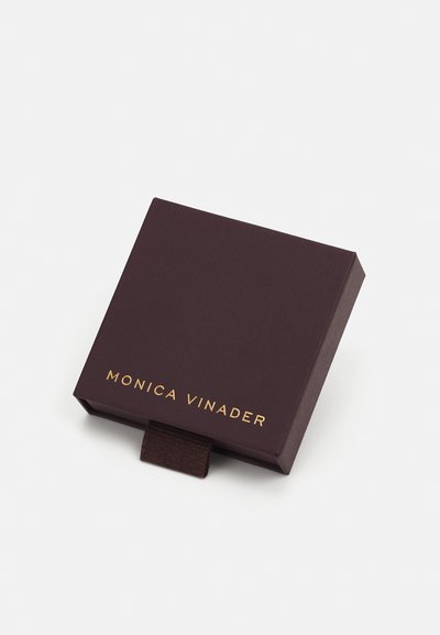 Brun tekstureret kasse med et guldfolieret brandnavn "MONICA VINADER" og en stoftrækklap til åbning. Kompakt og kvadratisk form.