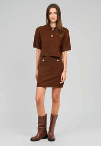 Ensemble coordonné en tricot marron comprenant un polo à manches courtes avec des accents de boutons et une jupe ajustée avec des poches latérales décoratives, finition texturée.