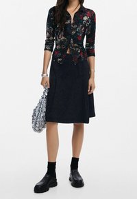 Black floral button-up shirt with long sleeves, paired with a dark skirt. Silver ruched bag and chunky black shoes complete the outfit.