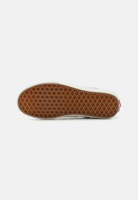 Sneakerzool met een bruine rubberen textuurpatroon; witte randen met een lichtgrijs ontwerp en een rode accent aan de hiel.