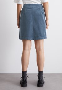 Falda mini de pana en azul apagado, con corte recto, bolsillos laterales y un dobladillo justo por encima de las rodillas, combinada con zapatos negros.