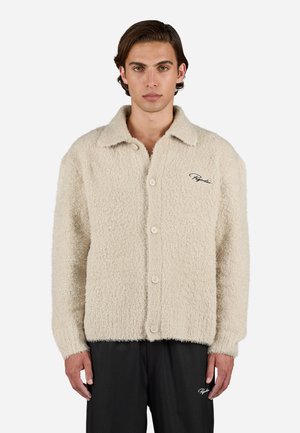 Beige, fluffy button-up shirt with a pointed collar and long sleeves. Features four buttons and a subtle embroidered logo on the chest.