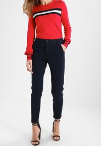 Punainen neule pimeys- ja valkoviiruilla, yhdistettynä slim-fit tummansinisiin housuihin. Raidalliset hihansuut ja korkeat korot täyden ovat asun.