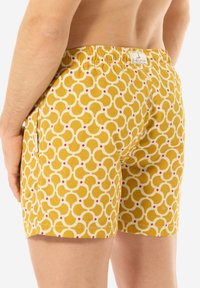Costumi da bagno caratterizzati da un motivo geometrico giallo e bianco, vita elastica e un'etichetta sul retro. Il materiale sembra leggero e liscio.
