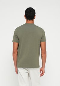 Zöld pamut rövid ujjú póló, kerek nyakkivágással és testhezálló szabással, világos színű nadrággal viselve. Egyszerű és egyszínű.