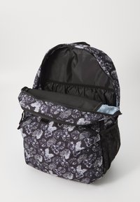 Black backpack with white floral and fern pattern, featuring a large zippered opening, a mesh side pocket, and a padded compartment inside.
