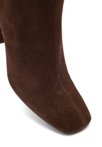 Gros plan sur une botte en daim marron à bout carré avec des coutures visibles le long de l'avant.