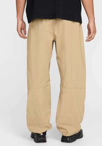 Pantalons larges couleur khaki avec une coupe décontractée, présentant une texture lisse et des accents cousus, portés avec des chaussures noires.