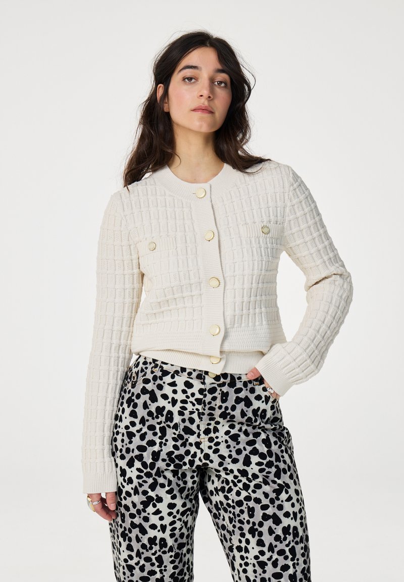 Crème cropped cardigan met een gestructureerd ruitpatroon, voorzien van gouden knopen en lange mouwen, gecombineerd met zwart-witte luipaardprintbroeken.