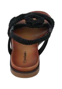 Zwarte gevlochten sandaal met een cirkelvormig geweven ontwerp, een platte bruine zool en flexibele banden, die een natuurlijke leertextuur toont.