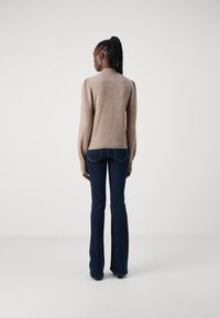 Beige strikkegenser med pufferm og ribbede kanter, brukt sammen med mørkeblå utsvingte bukser. Teksturen virker myk, med et subtilt mønster.