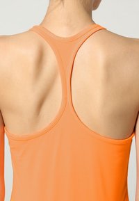 Canottiera sportiva arancione con design a racerback, caratterizzata da un tessuto liscio e elasticizzato e dettagli cuciti sul collo e sulle aperture per le braccia.
