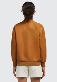 Giacca bomber marrone con finitura liscia, polsini e orlo a coste, e tasche laterali, caratterizzata da un colletto semplice e design monocolore.