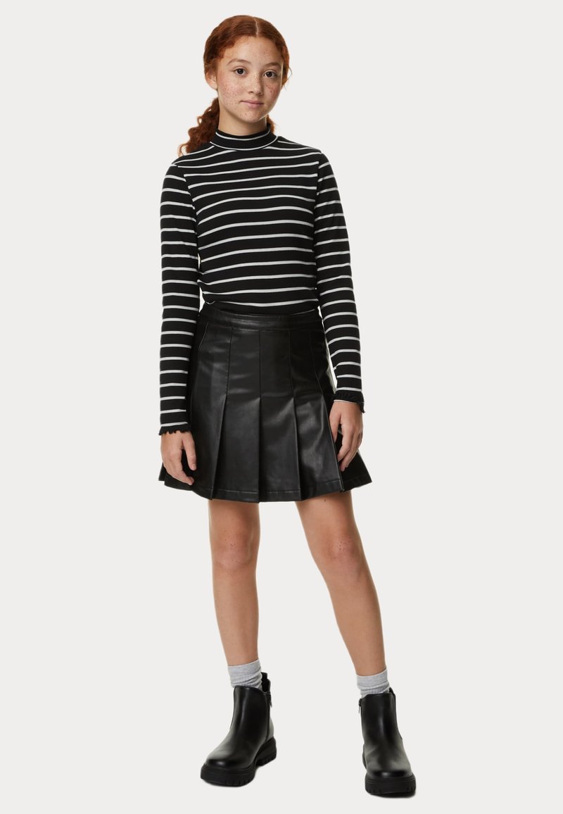 Top de cuello alto de rayas en blanco y negro con mangas largas, combinado con una falda plisada de piel sintética negra y botines negros.