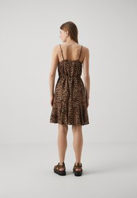 Haljina s uzorkom leoparda, tanke naramenice, uski korzet, rašireni suknja i nabran detalj oko struka. U kombinciji s smeškastim smešnim sandalama.
