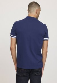 Polo shirt bleu marine à manches courtes, avec des accents en rayures blanches sur les poignets, fabriqué en coton lisse.
