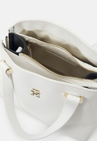 White leather handbag with gold hardware, zippered compartments, and a logo accent. Interior features beige lining and divided spaces.
